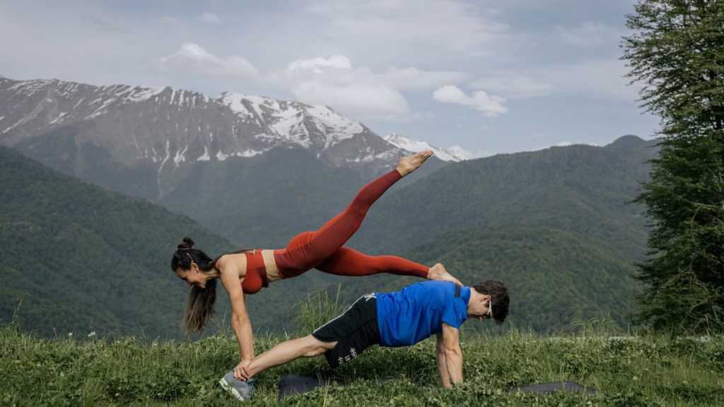 Couple doing yoga exercises outdoors with a breathtaking mountain view.